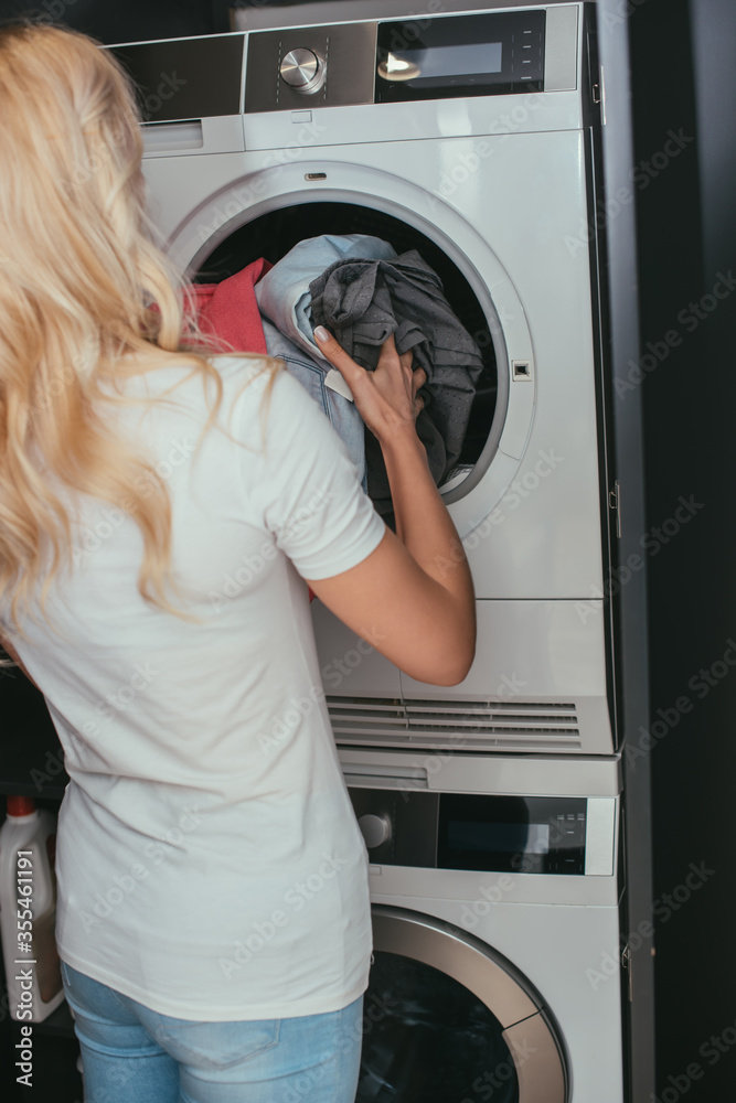 back view of blonde housewife putting laundry into washing machine