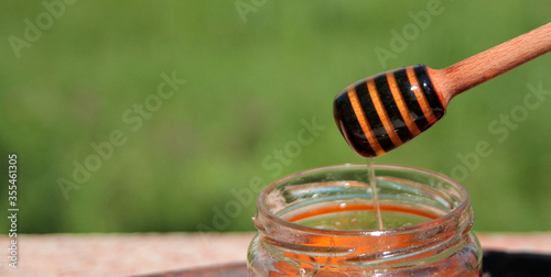Fotografía honey dipper with natural liquid honey, against a background of green trova and flowers