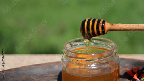 Cuadro en lienzo honey dipper with natural liquid honey, against a background of green trova and flowers