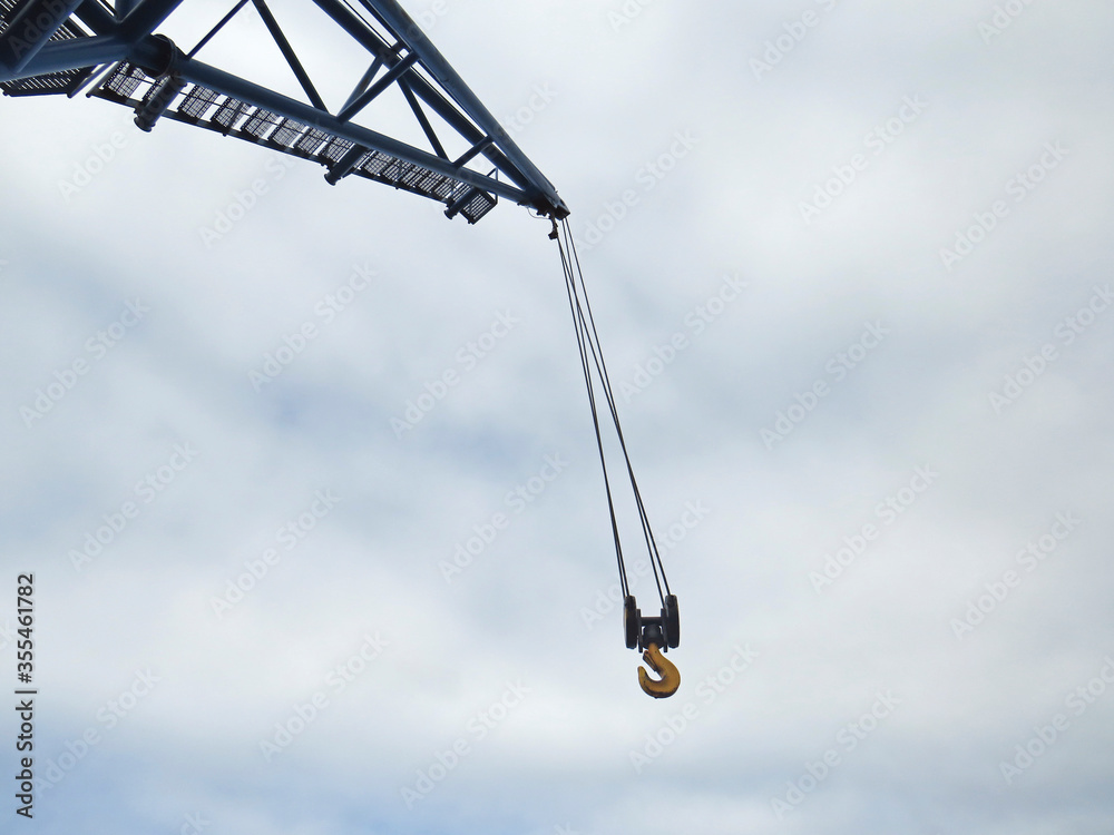 Close up of hanging crane hook and white cloudy sky. Industrial scene.Tall crane boom at construction site. Close up of hanging crane hook and white cloudy sky. Industrial scene.Tall crane boom at construction site.
