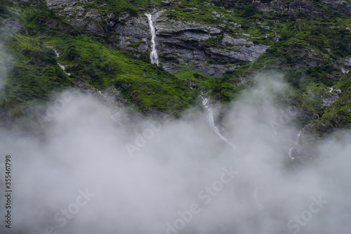Lush green   rocky mountains valley covered in clouds on a misty morning. Cloudy landscape with beautiful waterfalls captured during monsoon trek to Valley of Flowers National Park Uttarakhand  India.