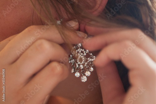 Beautiful unrecognizable bride in puts on diamond earring on her wedding day. High quality photo
