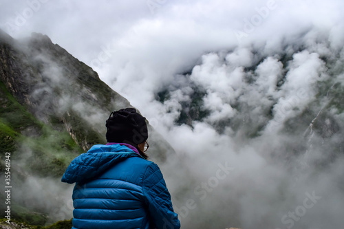 A solo hiker taking rest & enjoying mountain valley covered in clouds on a misty and rainy morning. Monsoon trek to Valley of Flowers National Park, Nanda devi biosphere reserve, Uttarakhand, India.