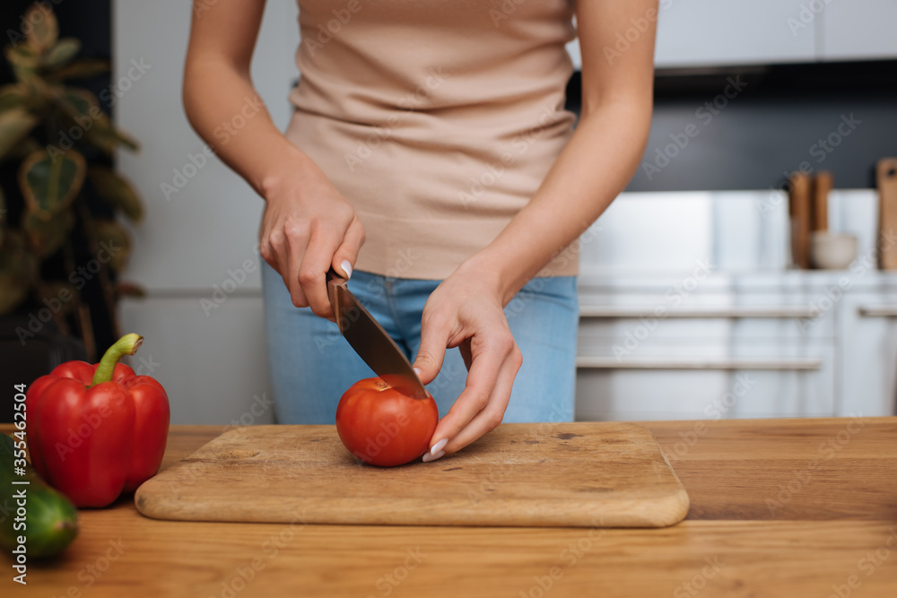 cropped view of young woman cutting fresh tomato on chopping board cropped view of young woman cutting fresh tomato on chopping board