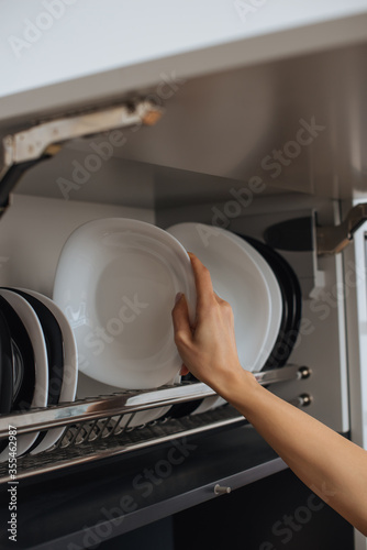 cropped view of housewife placing clean plate on rack in kitchen
