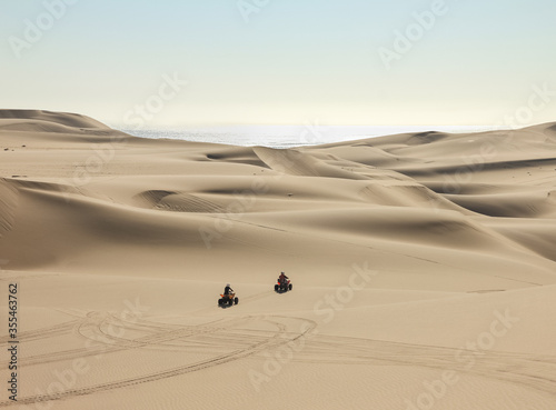 Quad driving people - two happy bikers in sand desert dunes at ocean coast beach, Africa, Namibia, Namib, Walvis Bay, Swakopmund.
