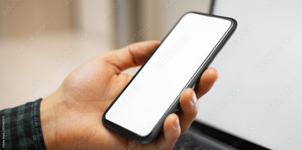 Close-up of male hand holding modern smartphone with white mockup.