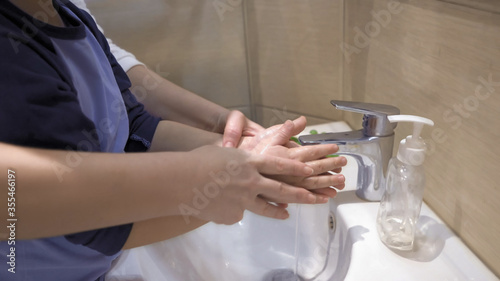 Mother and boy washing their hands together. Mom helps her son wash soap suds from his hands under running water. Parenthood concept.