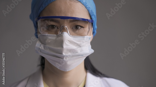 Tired doctor on gray background. Asian woman looking at camera. Abstract defocused image in motion.