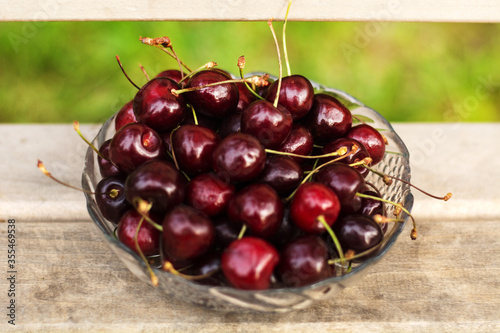 A transparent vase with cherries stands on a wooden bench.