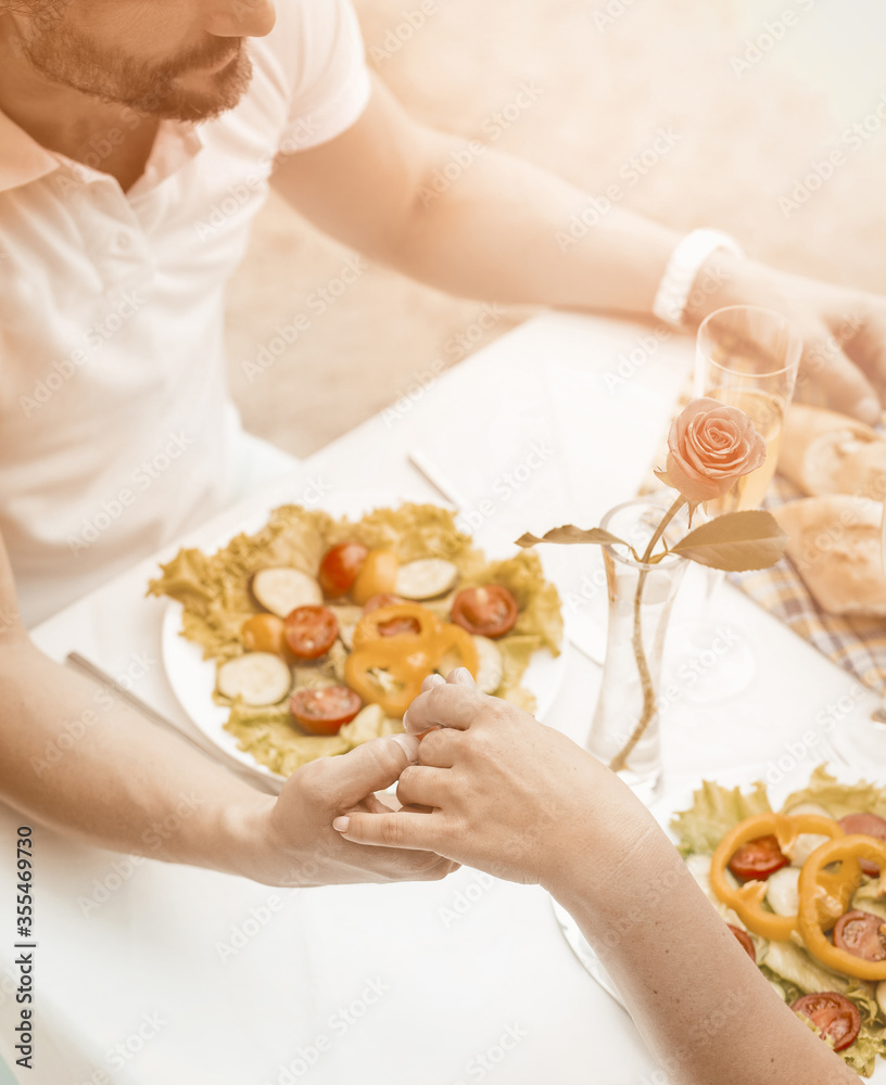 Obraz premium Lovely couple holding hands in beach cafe outdoor. Caucasian man and woman are happy to spend time with each other. Tenderness concept. Close up shot. High angle view. Toned image.