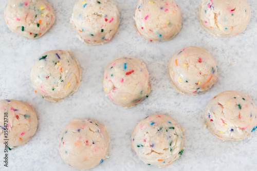 Birthday cake sprinkled edible cookie dough balls on white parchment paper.