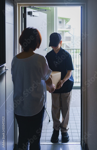 ネット通販の配達小包を届ける配達員とマンションの玄関先で受け取る主婦