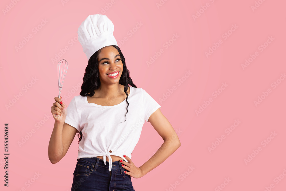Portrait of a smiling young female chef with whisker looking up, against pink studio background Portrait of a smiling young female chef with whisker looking up, against pink studio background
