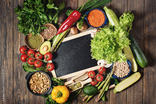 Legumes, lentils, chikpea and beans assortmen top view. Composition of different types of vegetables on wooden background. Black chalkboard with copy space photo