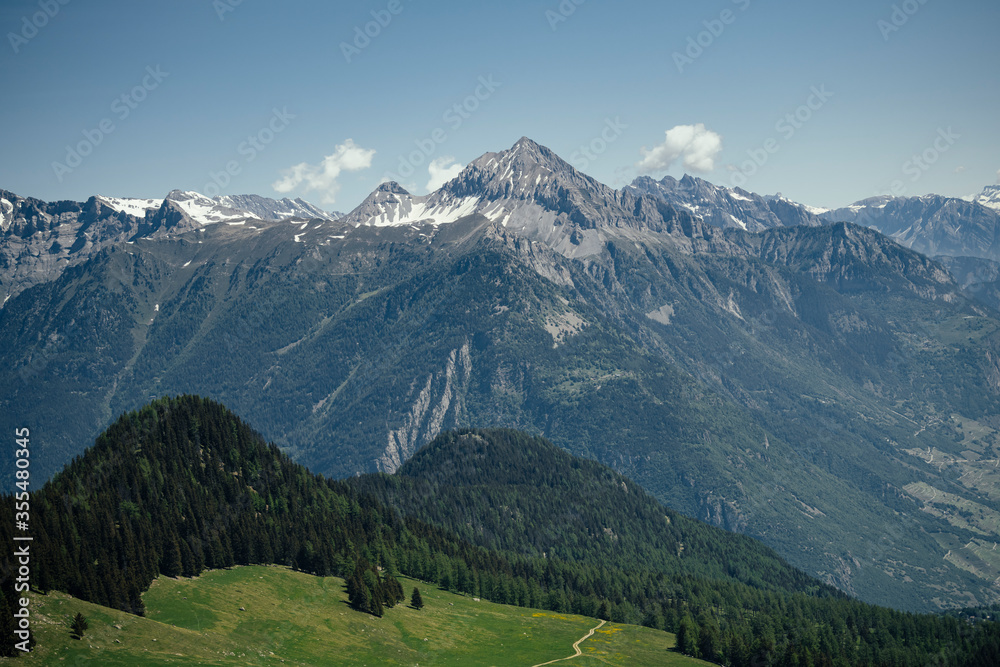 Alpine mountains, meadows and forests on a background of blue sky with clouds.