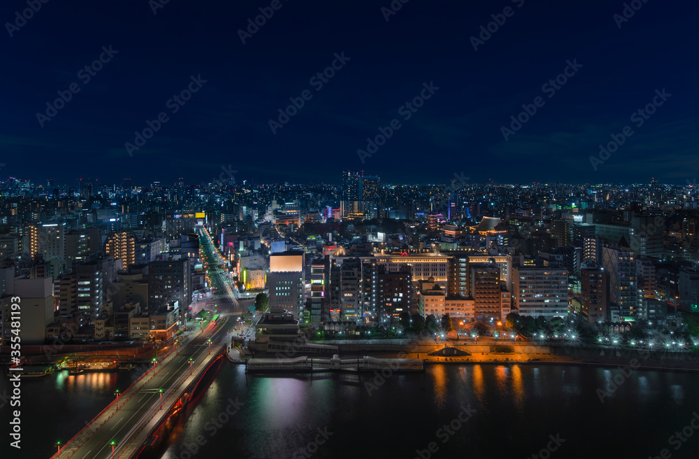 Aerial nocturn panoramic view of the Azumabashi bridge on Sumida river leading to the illuminated buildings and skyscrapers of Asakusa in Tokyo.