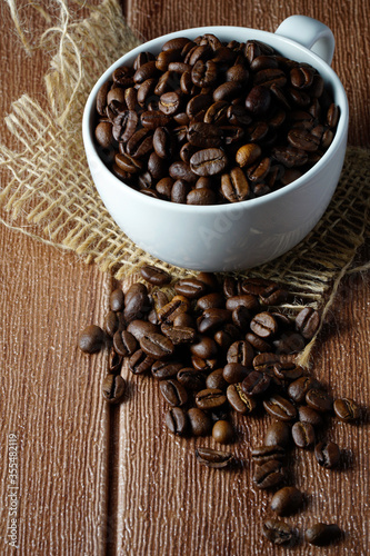 Coffee beans in a white cup on a wooden surface. Copyspace and international coffee day
