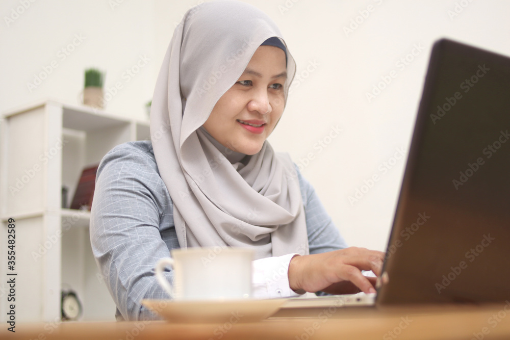 Happy young Asian muslim woman freelancer working on computer at home. Attractive businesswoman studying online, using laptop software, web surfing information or shopping in internet store Happy young Asian muslim woman freelancer working on computer at home. Attractive businesswoman studying online, using laptop software, web surfing information or shopping in internet store