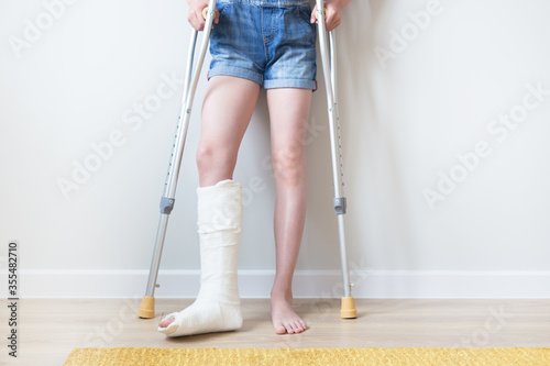 Close-up of children's feet, one leg is broken and in a cast, next to crutches. Light background. 
