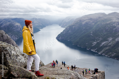 Fényképezés Smiling blonde woman hiker in yellow raincoat stays on the top of Preikestolen m
