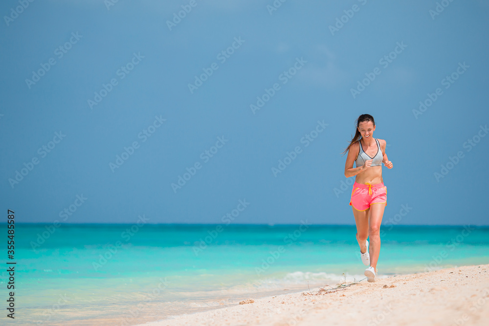 Fit young woman doing exercises on tropical white beach in her sportswear