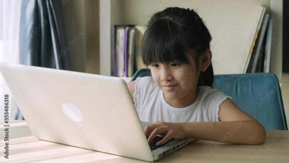 Homeschool Asian little young girl learning online class from school teacher by digital remote internet meeting due to coronavirus pandemic. Kid looking computer laptop screen that woman teaching. Homeschool Asian little young girl learning online class from school teacher by digital remote internet meeting due to coronavirus pandemic. Kid looking computer laptop screen that woman teaching.