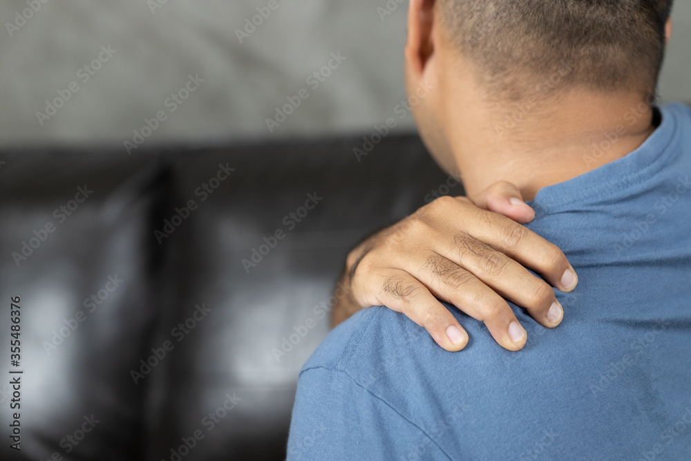 Man has neck pain, shoulder pain sitting on sofa at home Man has neck pain, shoulder pain sitting on sofa at home