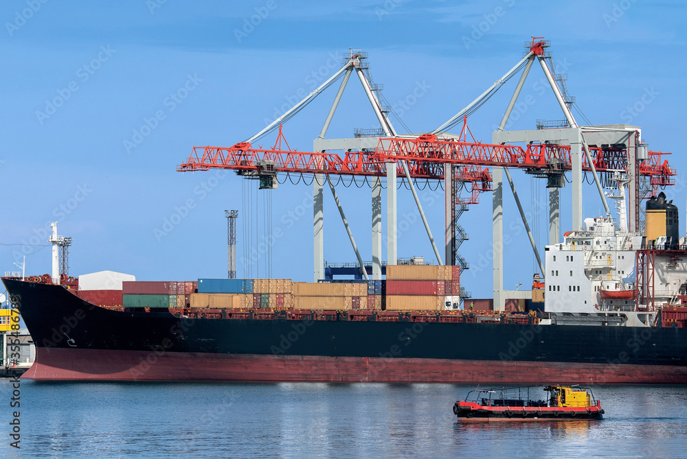Container ship is loading at the port. The longboat in the foreground looks very small. Container ship is loading at the port. The longboat in the foreground looks very small.
