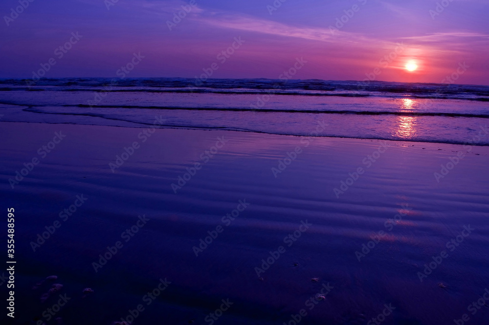 Fototapeta premium Seascape nature during a sunset on an empty ocean beach with gentle waves lapping at the shore. Very peaceful, as sun is above to dip below the horizon.