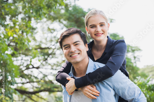 Boyfriend carrying his girlfriend in park. Wife is riding on back husband romantically.