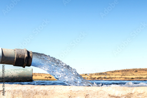 A Large stream of water gushing out of a pipe and filling a cement farm dam closeup photo
