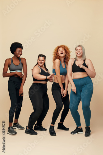 Body Positive. Diversity Women With Different Figure And Size Full-Length Portrait. Group Of Multi-Ethnic Girls In Sportswear Against Beige Background. Dancing And Sport As Lifestyle.