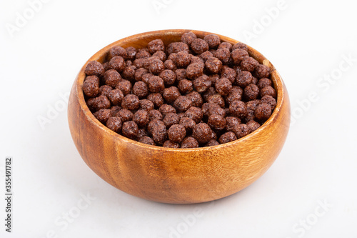 Wooden bowl with chocolate corn balls and spoon on white background