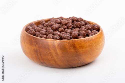 Wooden bowl with chocolate corn balls and spoon on white background