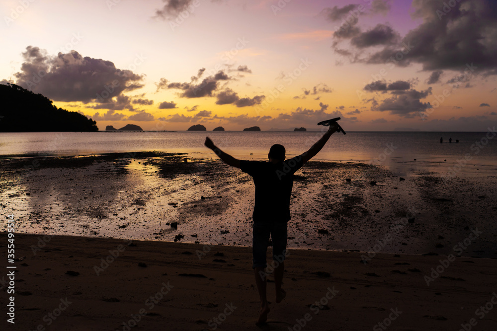 Silhouette of a man on the beach at sunset. Man rejoices meets the sunset