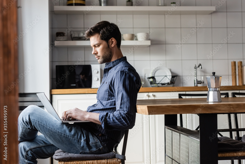 handsome freelancer working laptop with blank screen on kitchen with coffee pot during self isolation