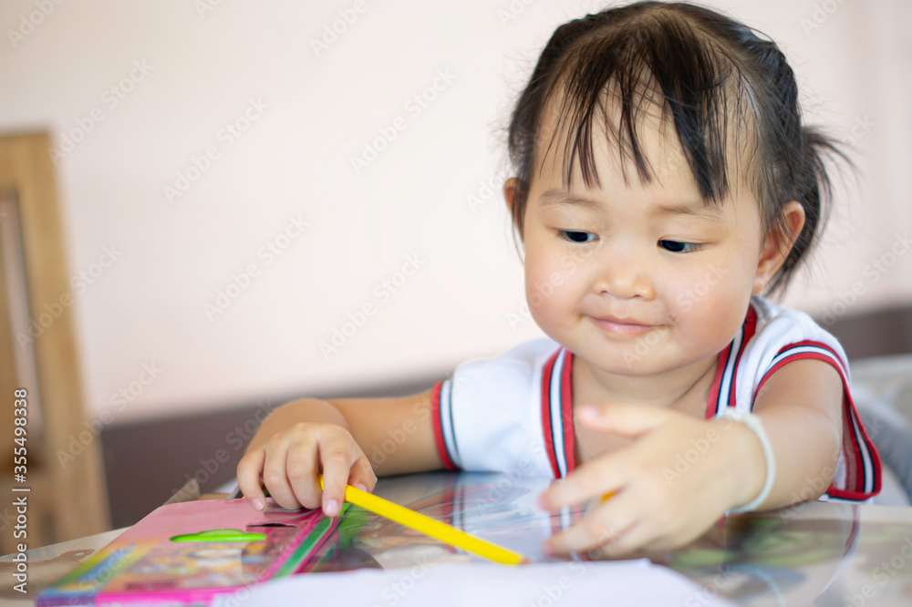 A young Asian female toddler with black hair is smiling and showing beautiful teeth.She happily with Colored pencils.And copy space. A young Asian female toddler with black hair is smiling and showing beautiful teeth.She happily with Colored pencils.And copy space.
