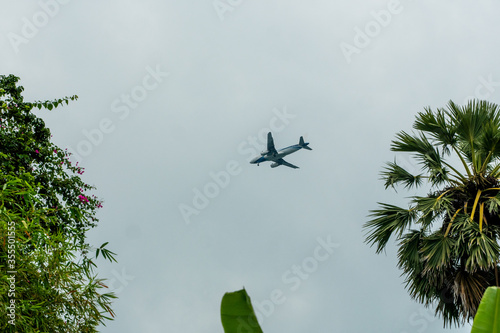 Plane flying in a cloudy sky and preparing to land on a tropical island.