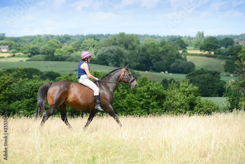 Pretty young woman and her bay horse enjoy a peaceful ride across the Shropshire countryside on a summers day.
