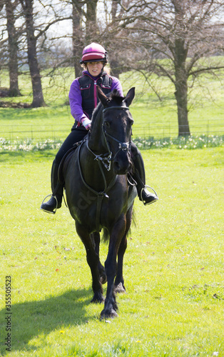 Pretty female rider and her black horse enjoy a ride in the English countryside on a summers day.
