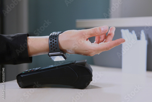 Payment without money .Online payment for purchases or services. Hand with a watch and a payment terminal close-up. An unrecognizable photo. Copy of the space.