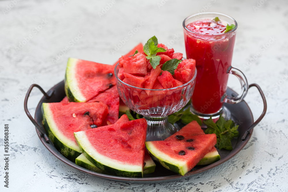 Pieces of ripe watermelon and a glass of watermelon juice on a dish and a light texture background. Pieces of ripe watermelon and a glass of watermelon juice on a dish and a light texture background.