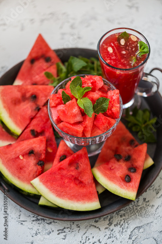 Pieces of ripe watermelon and a glass of watermelon juice on a dish and a light texture background.