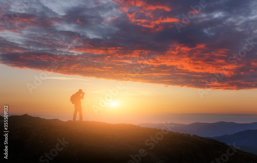 Silhouette of Nature photographer in the action on top under sunlight. climber Man under a fantastic colorful clouds, landscape at Sunset. Scenic image of highland in sunlit. Travel conception.