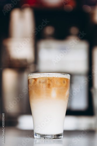 Glass with coffee, milk and ice on cafe background