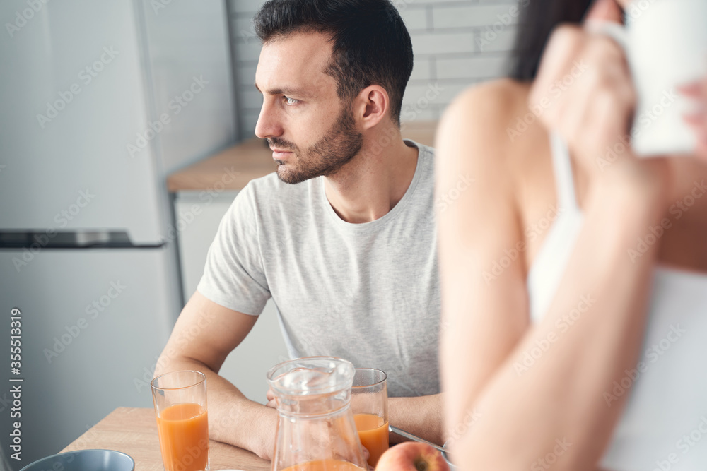 Unhappy tired man having breakfast at home with his wife Unhappy tired man having breakfast at home with his wife