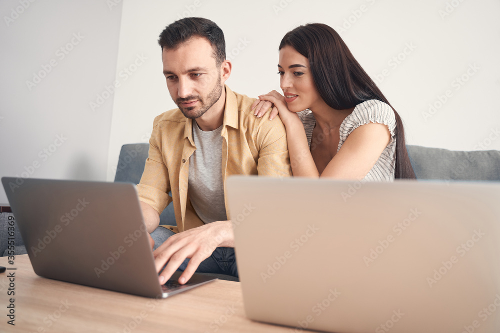 Young woman watching her husband working online on a notebook
