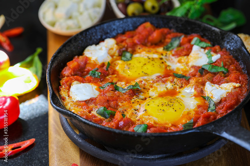 Shakshuka. Fried eggs in tomato sauce, with tomatoes and hot peppers, in a cast-iron frying pan.