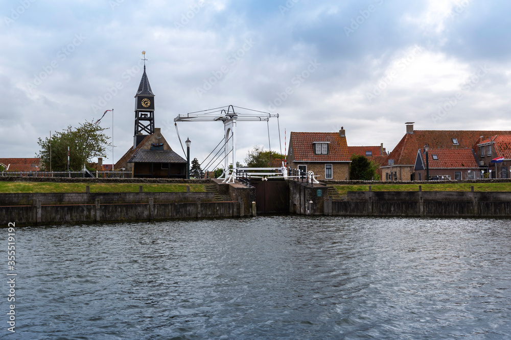 Netherlands - Hindeloopen coast with fairways to the canals of the city of Hindeloopen. On the left is a church with a wooden tower and clock, on the right are houses.